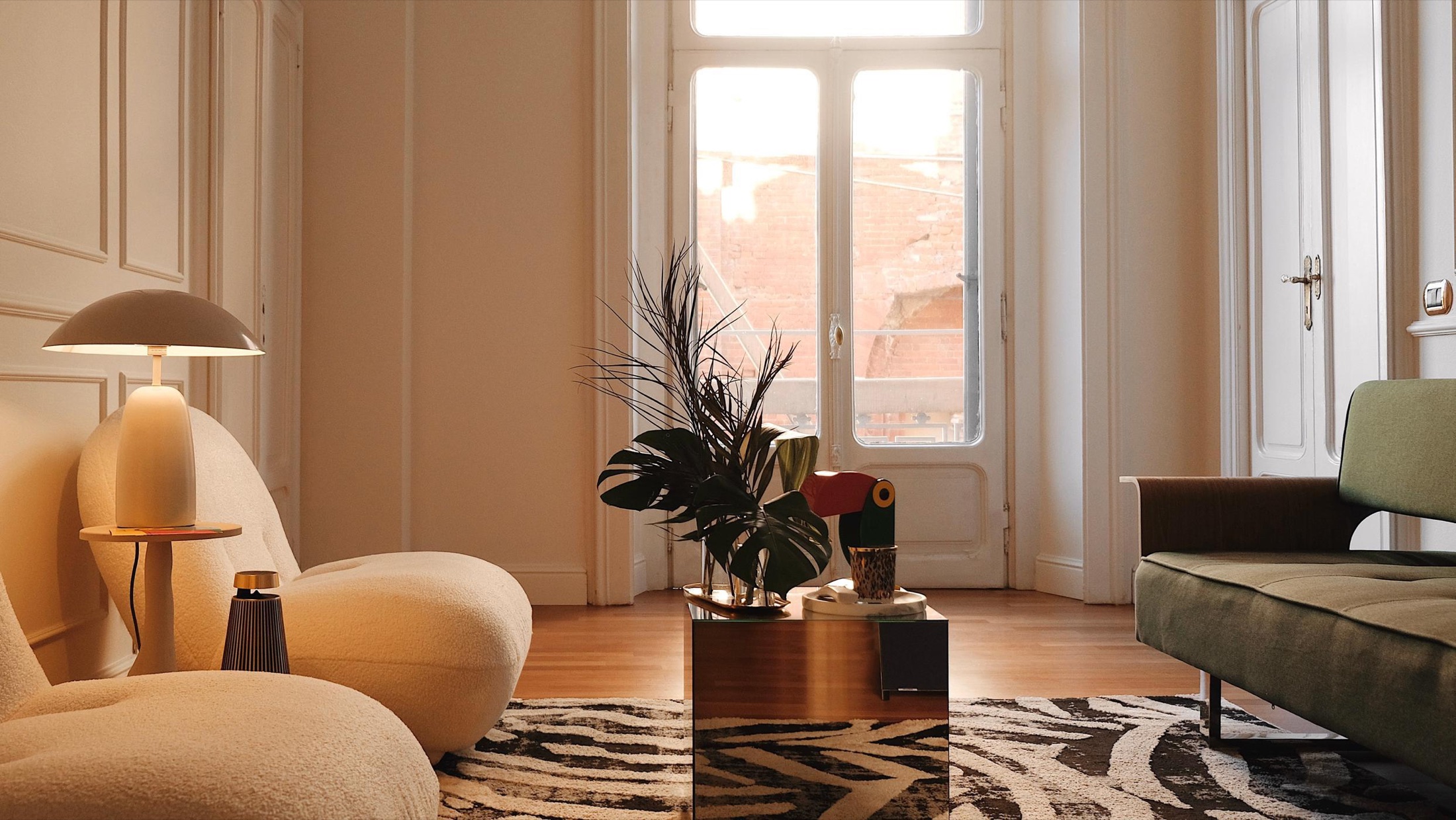 Natural light across the Salotto lounge, with ivory armchairs, an olive sofa, a mirrored table and historic window shutters